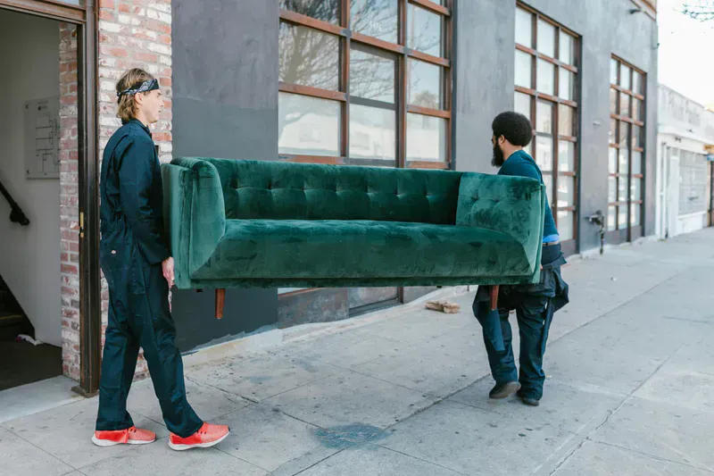 Mover carrying an old sofa out of a house for furniture removal in Bangor, Maine